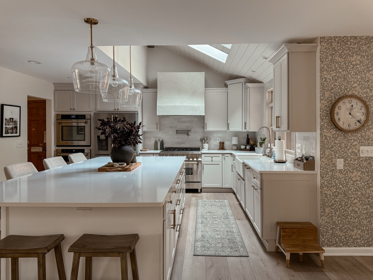 A white kitchen with a large island and glass pendant lights